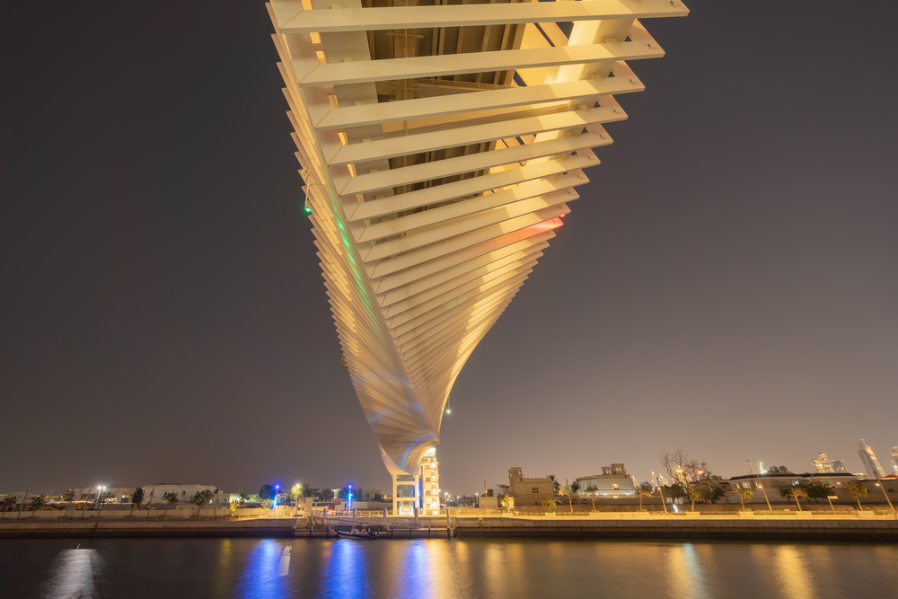 Twisted Bridge. Structure of architecture with lake or river, Dubai Downtown skyline, United Arab Emirates or UAE. Financial district and business area in urban city at night.