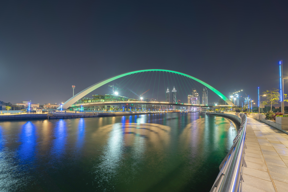 Tolerance bridge. Structure of architecture with lake or river, Dubai Downtown skyline, United Arab Emirates or UAE. Financial district and business area in urban city at night.