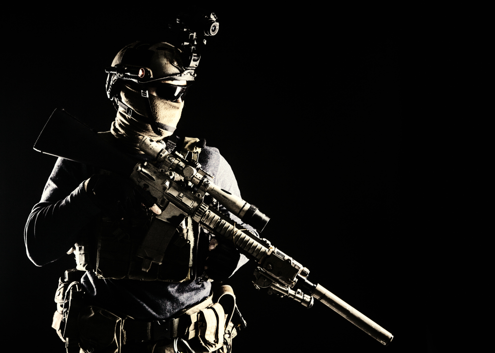Army elite troops marksman, special operations forces sniper wearing mask and glasses, night-vision or infrared thermal imaging device on helmet, holding service rifle with optical sight and silencer. Army marksman with sniper rifle in darkness