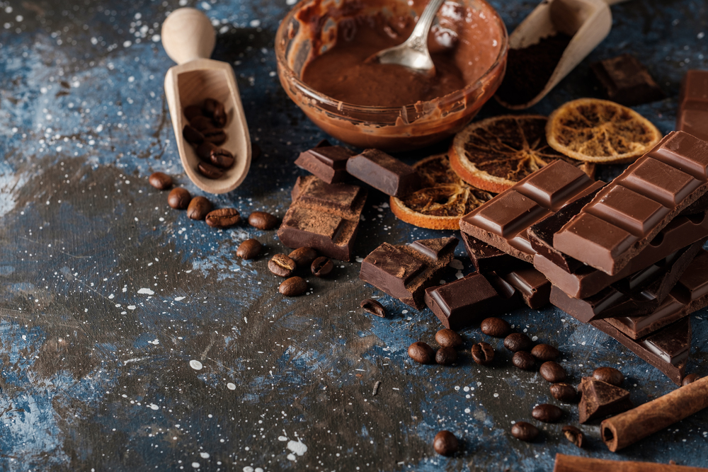 Dark and milk chocolate bars with dry orange slices, cinnamon sticks and coffee beans on blue background