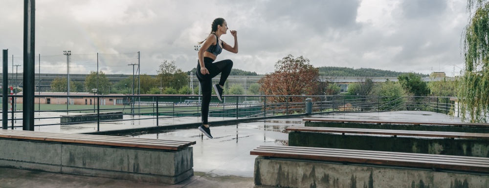 Young girl jumping on benches doing outdoor training on rainy day. Girl jumping on benches doing training
