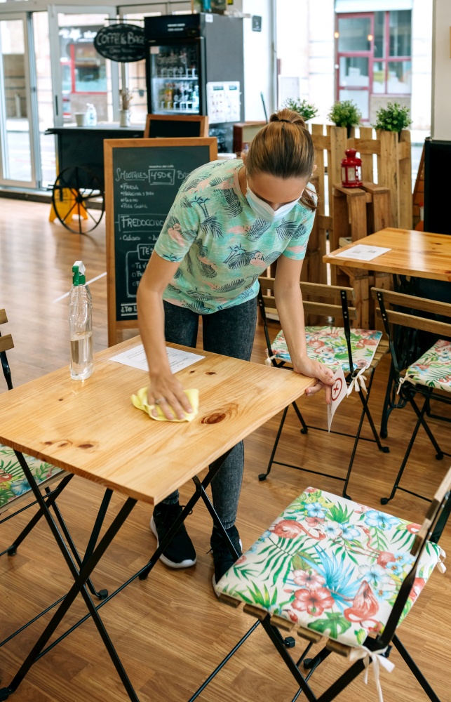 Waitress disinfecting tables in a coffee shop due to coronavirus. Waitress disinfecting tables in a coffee shop