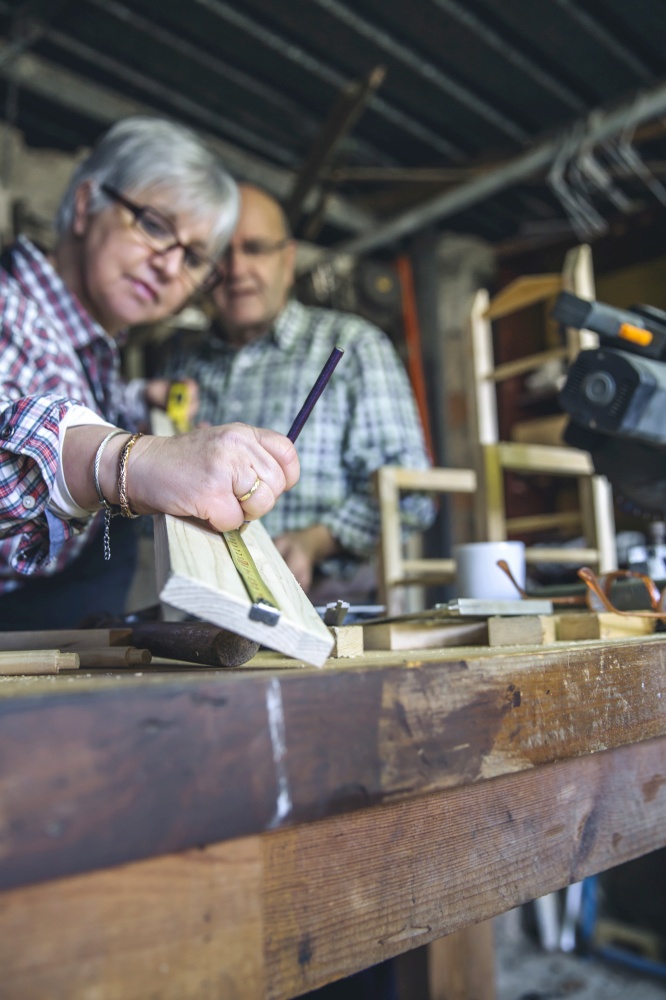 Senior couple working in a carpentry workshop. Selective focus on hand in foreground. Senior couple in a carpentry