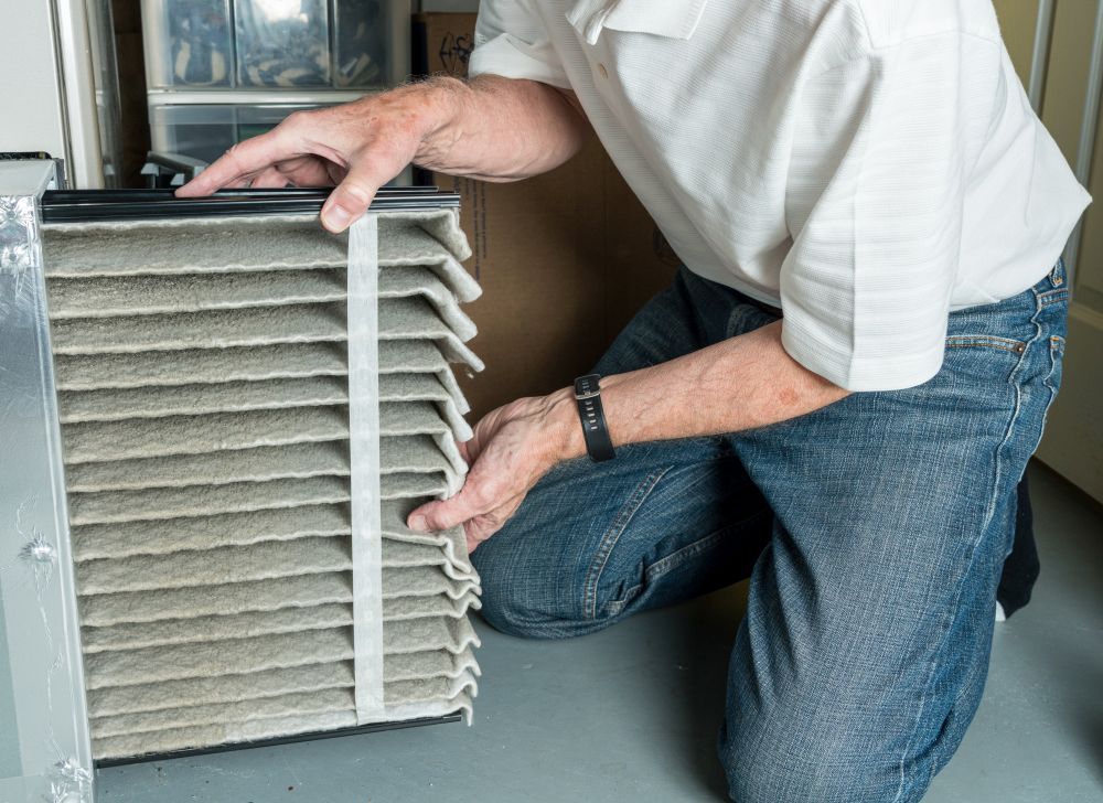 Senior caucasian man changing a folded dirty air filter in the HVAC furnace system in basement of home. Senior man changing a dirty air filter in a HVAC Furnace