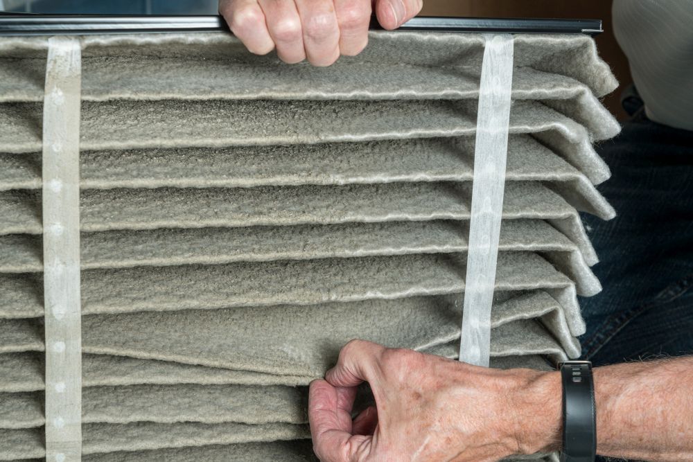 Senior caucasian man looking at the dust in folded dirty air filter in the HVAC furnace system in basement of home. Senior man changing a dirty air filter in a HVAC Furnace