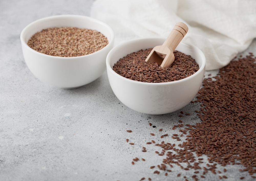 Bowl of raw natural organic linseed flax-seed with spoon and powder on light background with linen cloth.