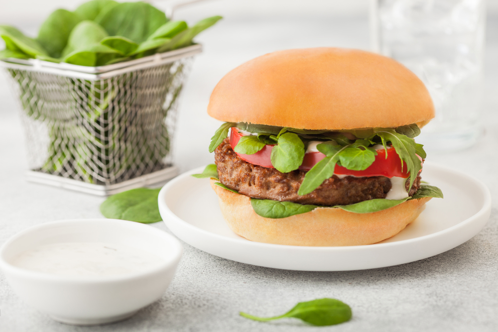 Healthy vegetarian meat free burger on round ceramic plate with vegetables and spinach on light background..