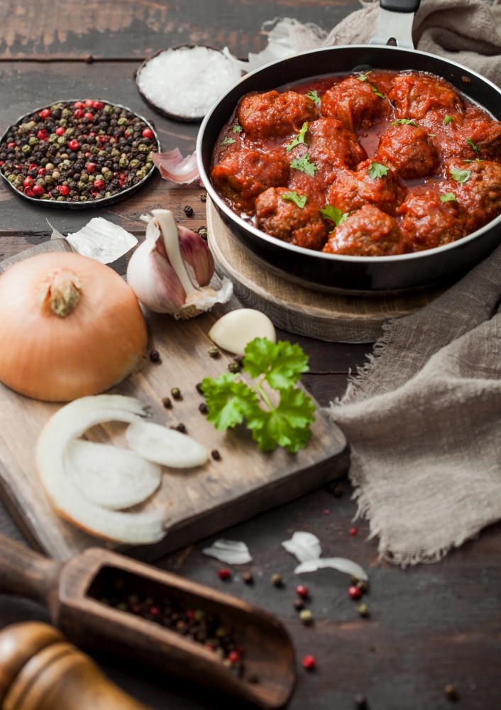 Beef traditional meatballs in tomato sauce in frying pan with pepper, garlic and parsley with onion and salt on wooden background.