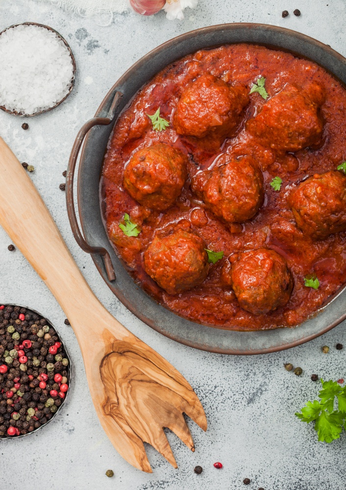 Meatballs in tomato sauce with pepper, garlic and parsley on light table with utensils. Top view