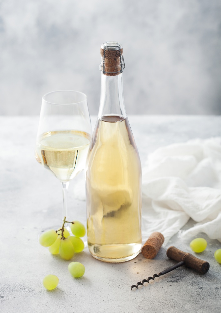 Bottle and glass of white homemade wine with grapes and corkscrew with linen cloth on light table background.
