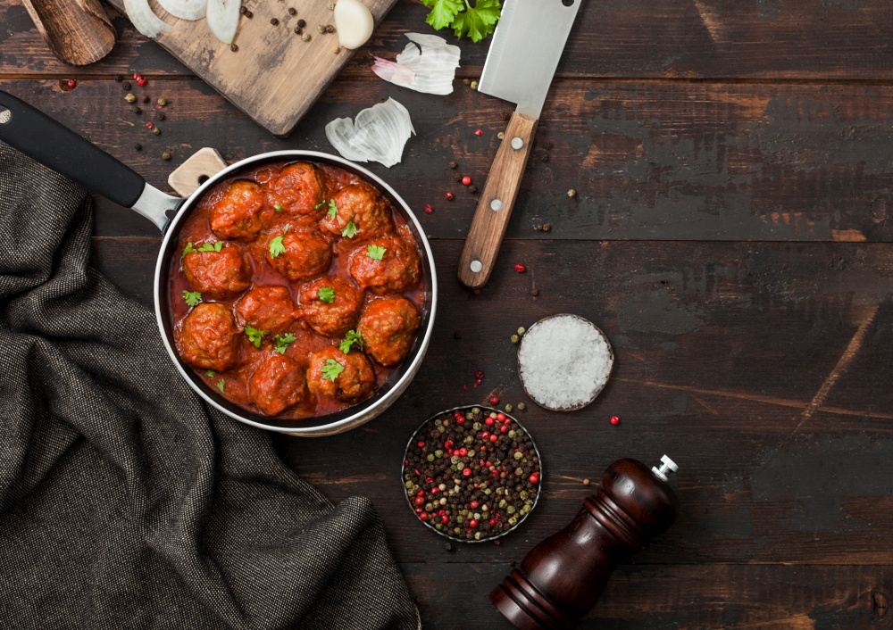 Beef spicy meatballs in tomato sauce with pepper, garlic and parsley with onion and cleaver on dark wooden background. Space for text