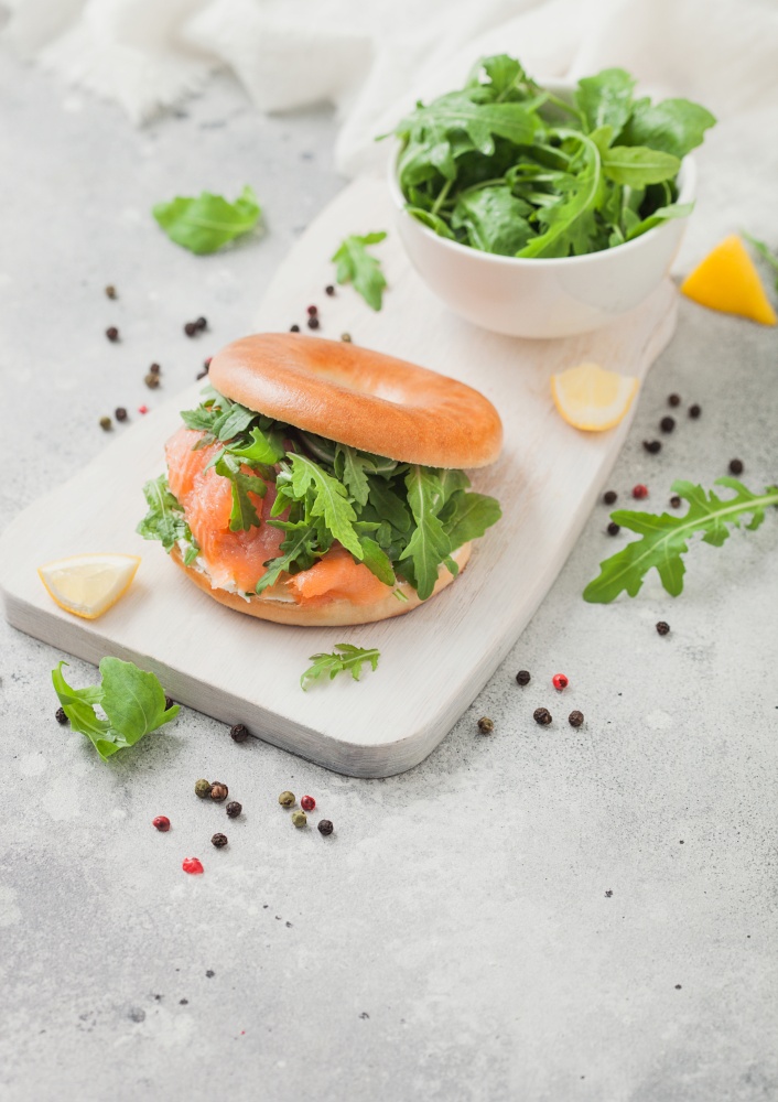 Bagel and salmon sandwich with cream cheese and wild rocket in white bowl and lemon with pepper.