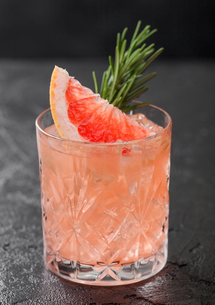Grapefruit and rosemary drink, alcohol or non-alcohol cocktail in glass with ice cubes on black background. Macro