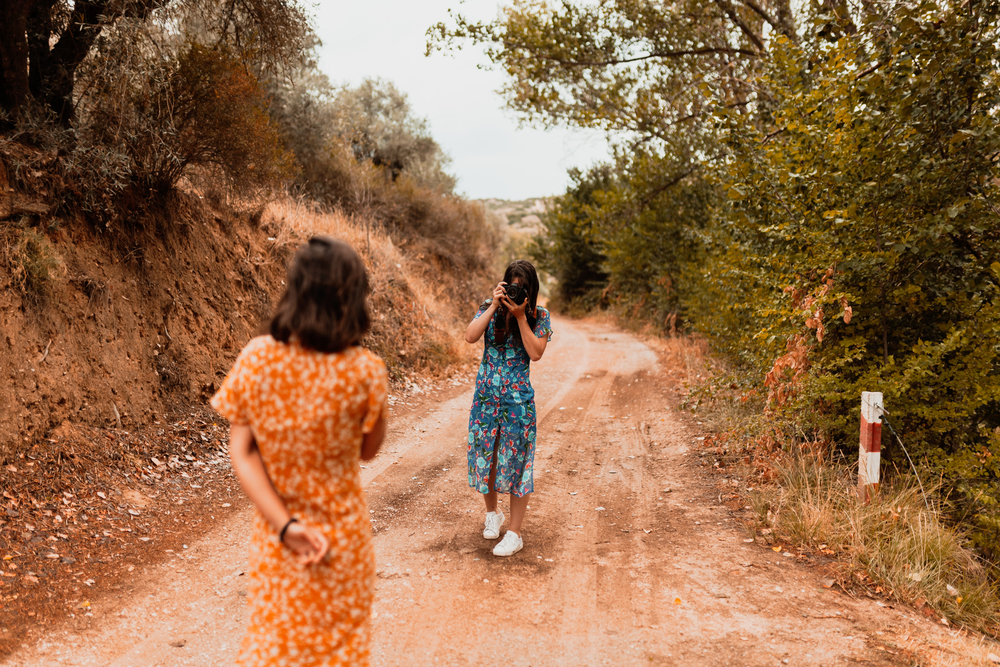 Two young women taking photos on a path near a forest