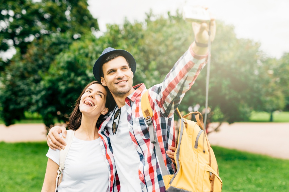 Joyful female and her best friend having excursion in park, making selfie, having happy expressions while hugging. Female and male walking on street. Positive emotions, facial expressions concept