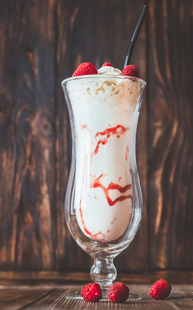 Glass of raspberry milkshake on the wooden background