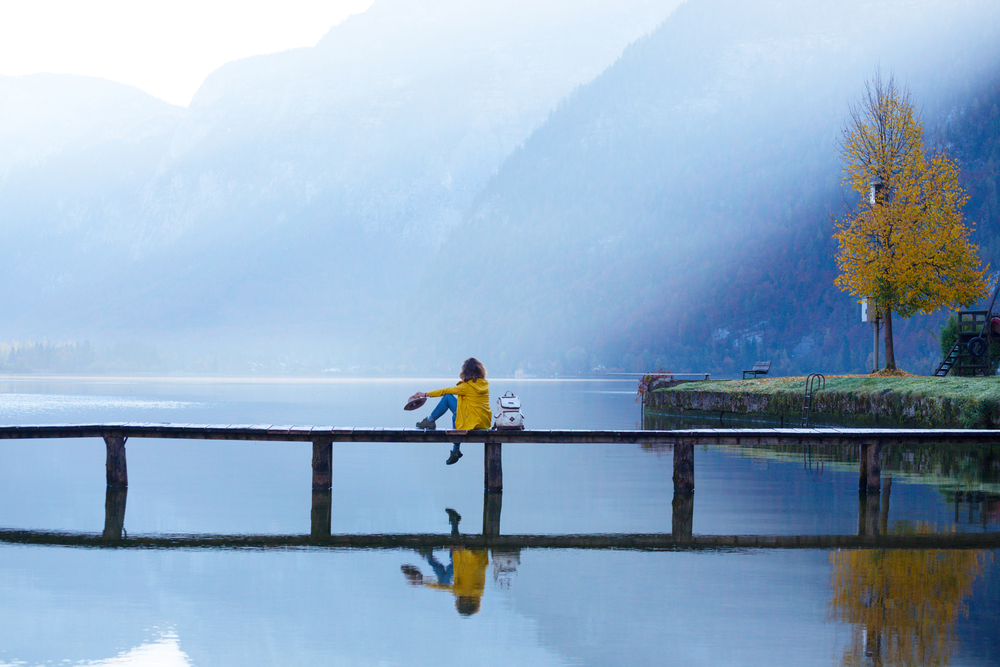 girl tourist in a hat and with a backpack sitting on a wooden bridge on a mountain lake in the early morning. beautiful landscape and reflection. Hallstatt
