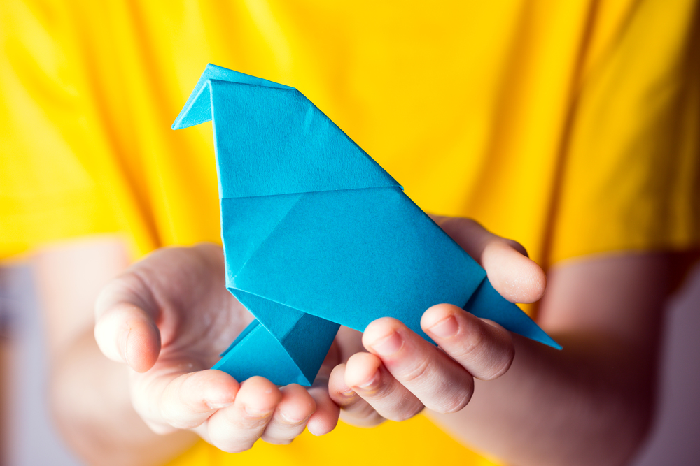 girl holding a blue origami bird in her hands on a yellow background. interesting hobby