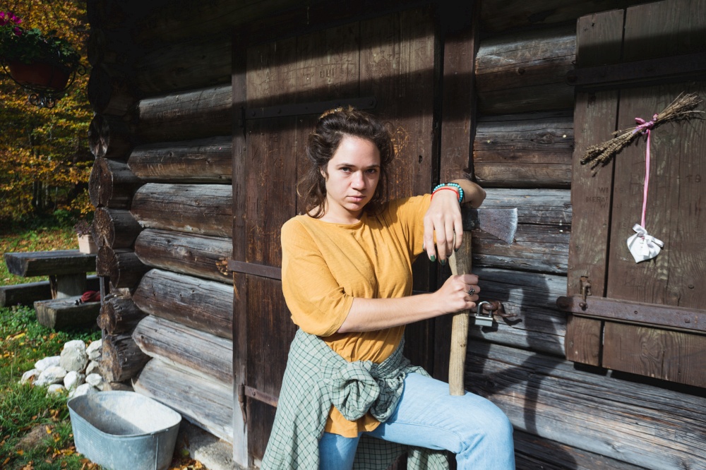 girl with an ax near a wooden house in the mountains