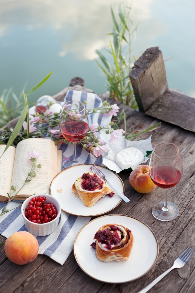 Summer still life-   picnic on a wooden pier. wine, sinabones, peaches, a book with a lake view