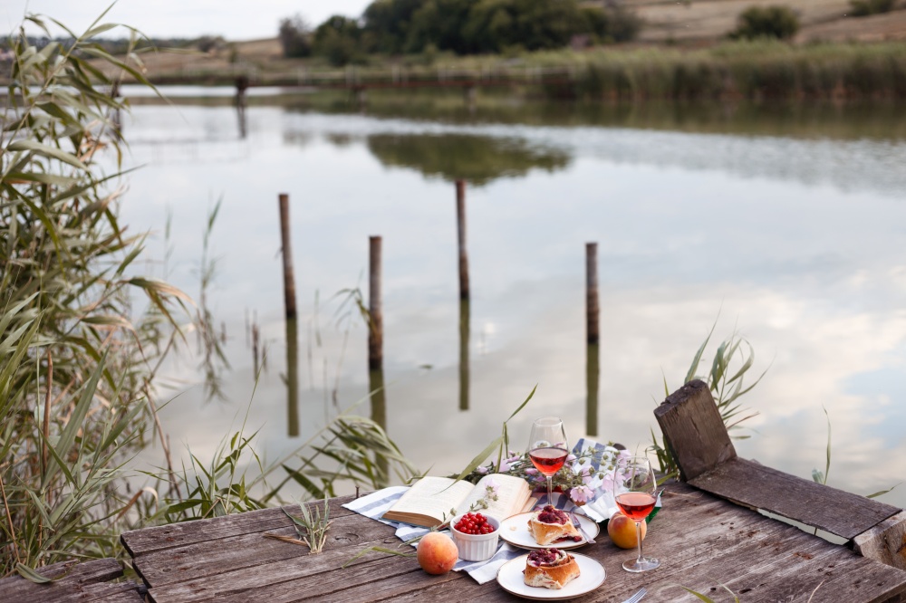 Summer still life-   picnic on a wooden pier. wine, sinabones, peaches, a book with a lake view