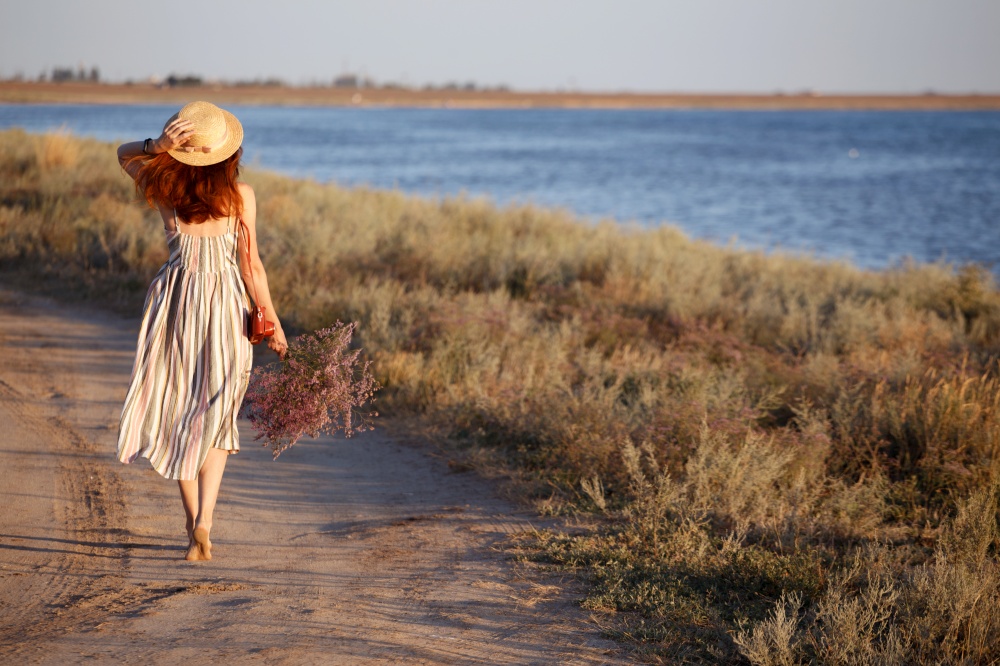 a girl in a hat and with a bouquet walks along the seashore