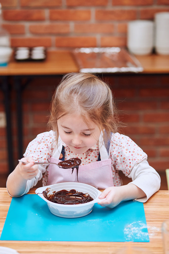 Little girl smelling the melted chocolate and cocoa. Kid taking part in baking workshop. Baking classes for children,  aspiring little chefs. Learning to cook. Combining and stirring prepared ingredients. Real people, authentic situations