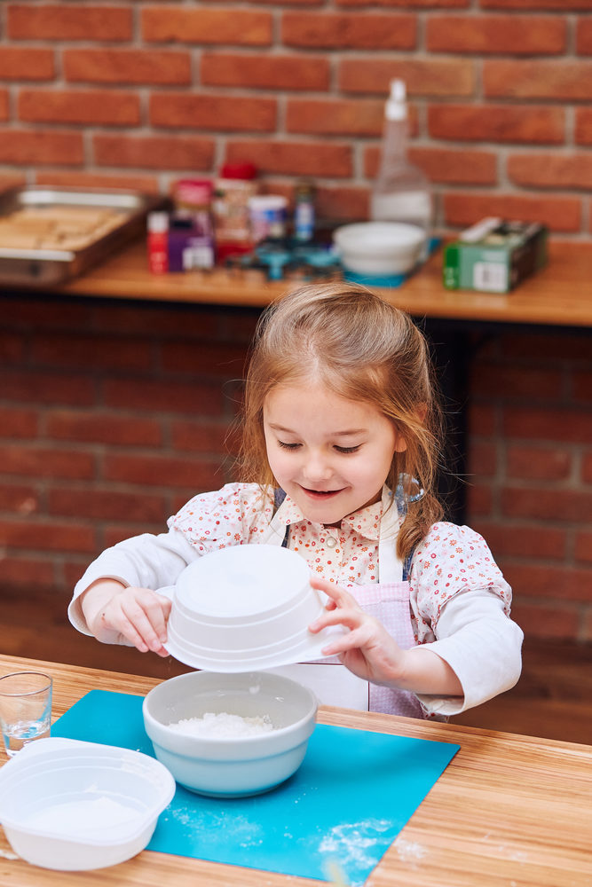 Little girl combining the ingredients for baking the cake. Kid taking part in baking workshop. Baking classes for children, aspiring little chefs. Learning to cook. Combining and stirring prepared ingredients. Real people, authentic situations