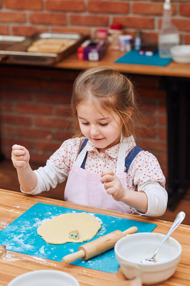 Little girl cutting the dough to heart shapes cookies. Kid taking part in baking workshop. Baking classes for children, aspiring little chefs. Learning to cook. Combining and stirring prepared ingredients. Real people, authentic situations