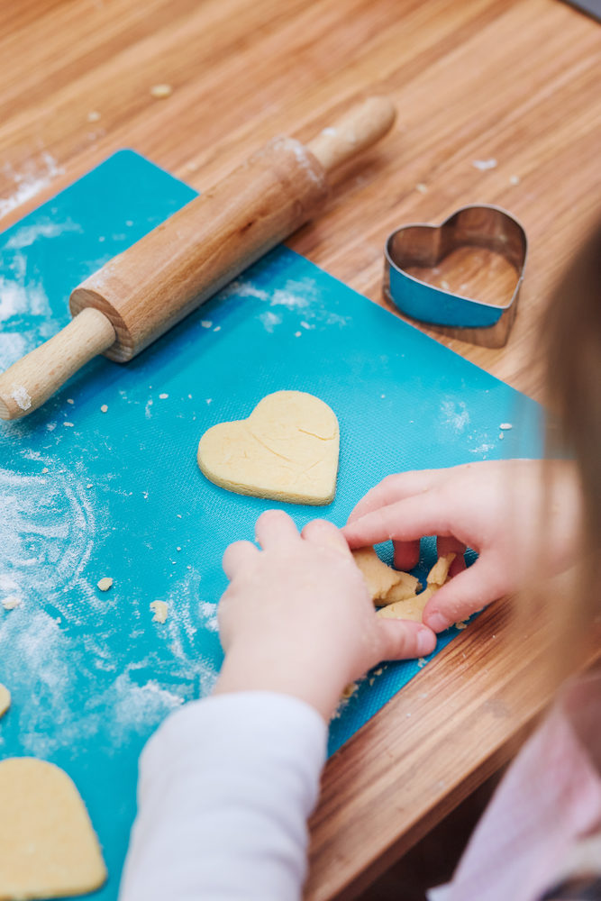 Little girl cutting the dough to heart shapes for the cookies. Kid taking part in baking workshop. Baking classes for children, aspiring little chefs. Girls learning to cook. Combining and stirring prepared ingredients. Real people, authentic situations