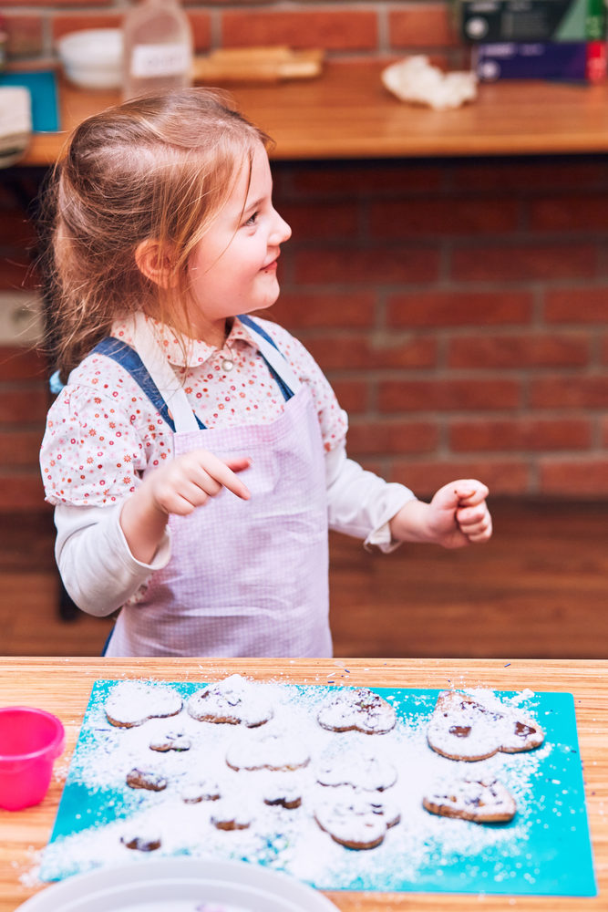 Little girl enjoying her baked cookies. Decorating cookies with colorful sprinkle and icing sugar. Kid taking part in baking workshop. Baking classes for children, aspiring little chefs. Learning to cook. Combining and stirring prepared ingredients. Real people, authentic situations