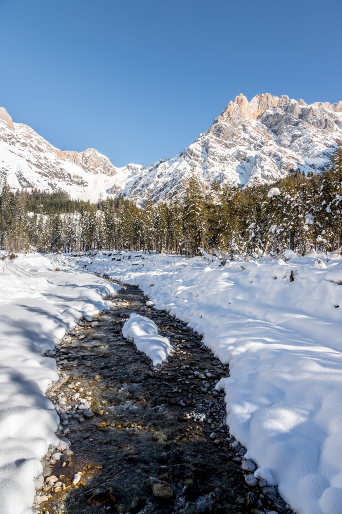 Idyllic winter landscape: stunning mountain range, beautiful river, snowy trees and blue sky