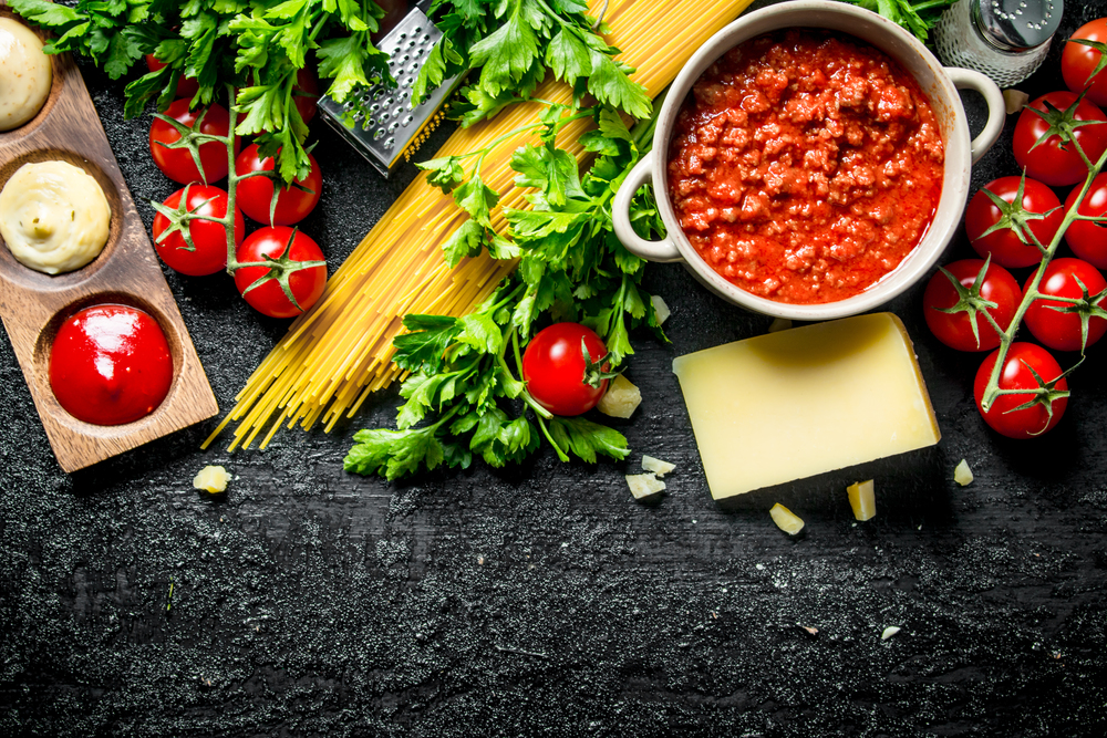 Pasta background. Dry spaghetti with Bolognese sauce,herbs, tomatoes and cheese. On black rustic background. Pasta background. Dry spaghetti with Bolognese sauce,herbs, tomatoes and cheese.