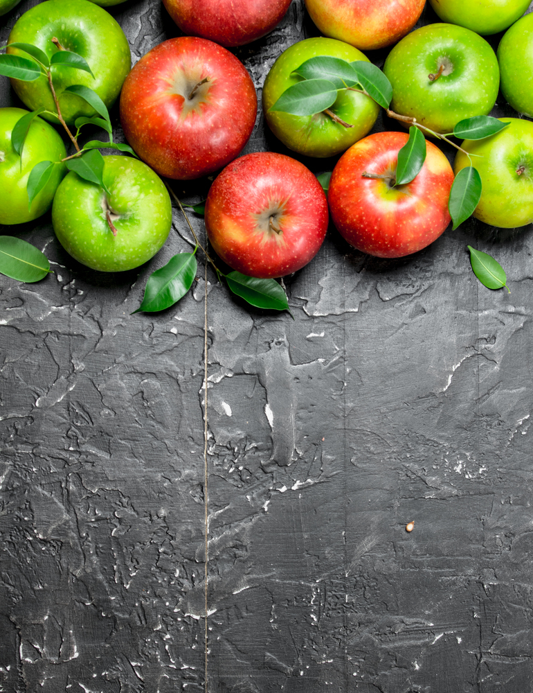 Whole green and red apples with leaves. On black rustic background.. Whole green and red apples with leaves.