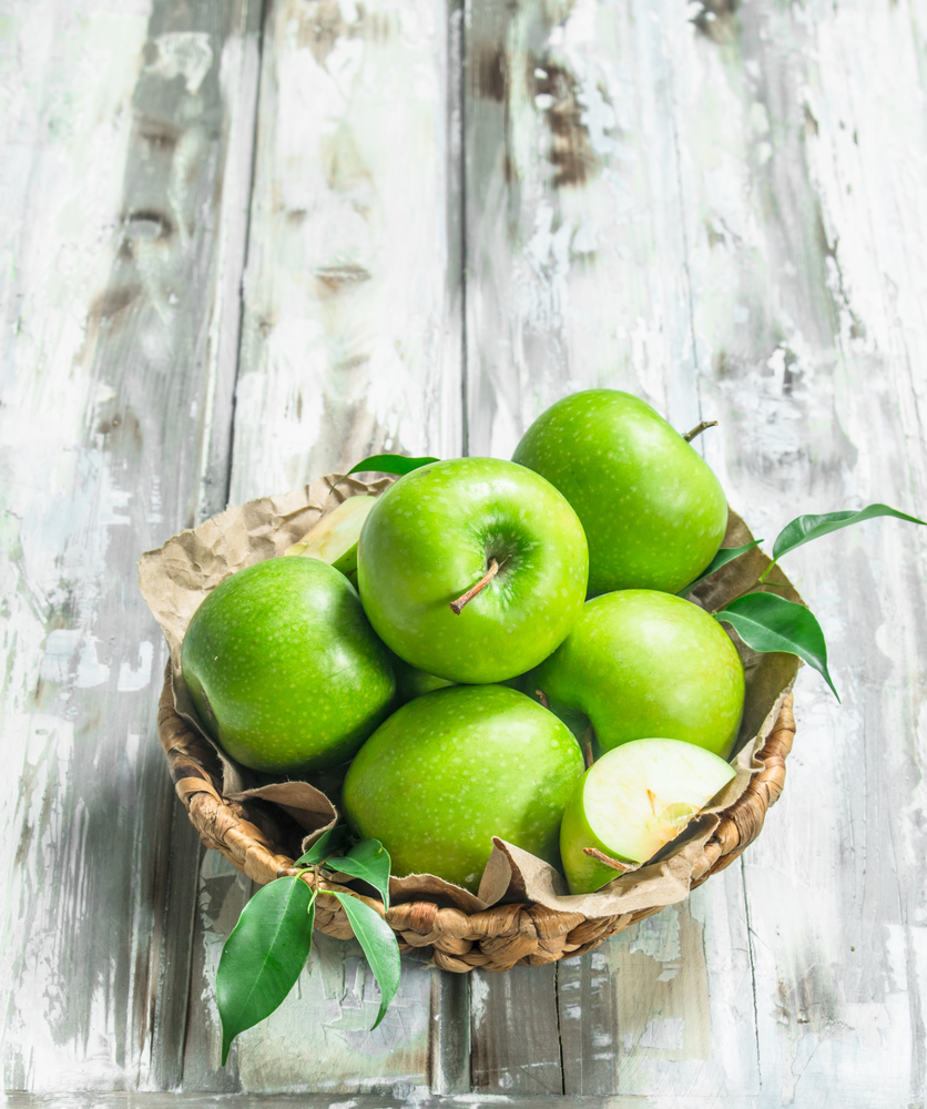 Green apples in the basket. On a white wooden background.. Green apples in the basket.