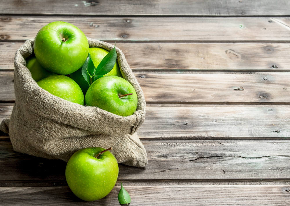 Juicy green apples in an old bag. On grey wooden background.. Juicy green apples in an old bag.