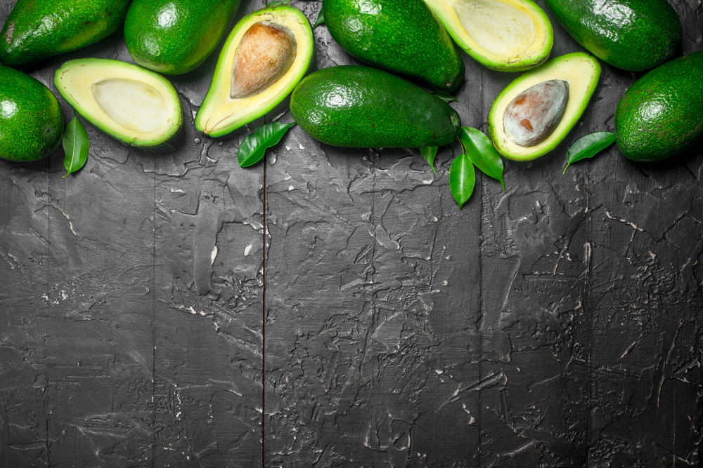 Avocado and avocado slices with leaves. On black rustic background.. Avocado and avocado slices with leaves.