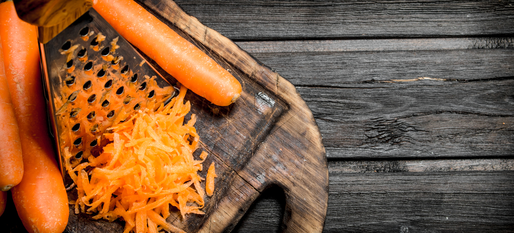 Grated carrots on a cutting Board with a grater. On wooden background. Grated carrots on a cutting Board with a grater.