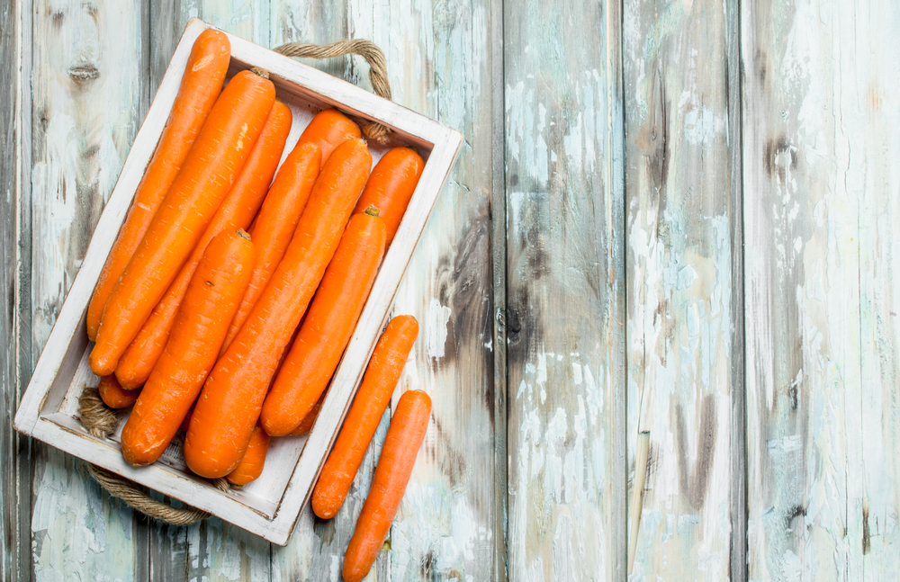 Ripe carrots in a wooden tray. On wooden background. Ripe carrots in a wooden tray.