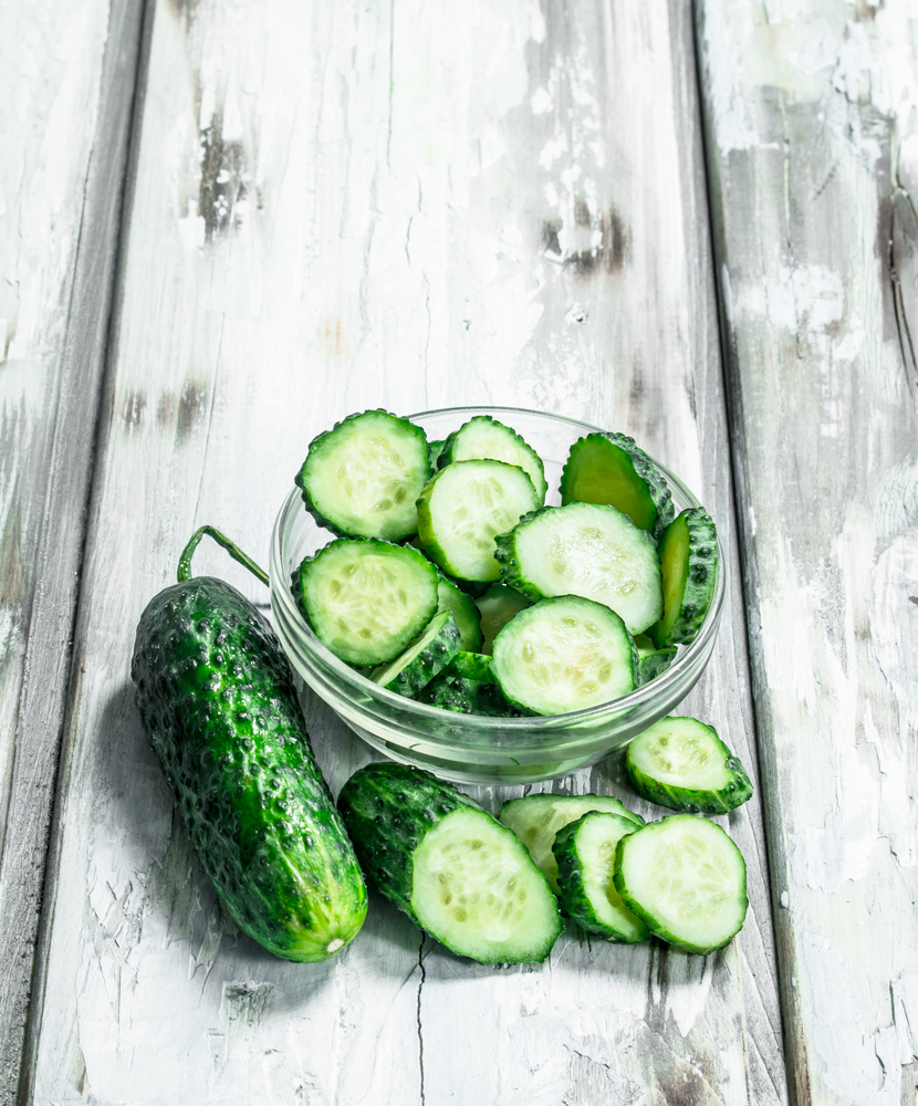 Pieces of fresh cucumbers in the bowl. On white wooden background. Pieces of fresh cucumbers in the bowl.
