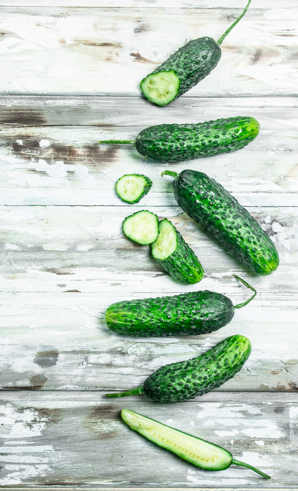 Whole and sliced cucumbers. On wooden background. Whole and sliced cucumbers.