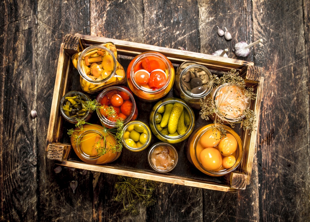 Preserves mushrooms and vegetables in a box. On a wooden background.. Preserves mushrooms and vegetables in a box.