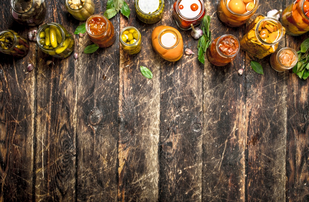 Different preserved vegetables from vegetables and mushrooms in glass jars. On a wooden background.. Different preserved vegetables from vegetables and mushrooms in glass jars.