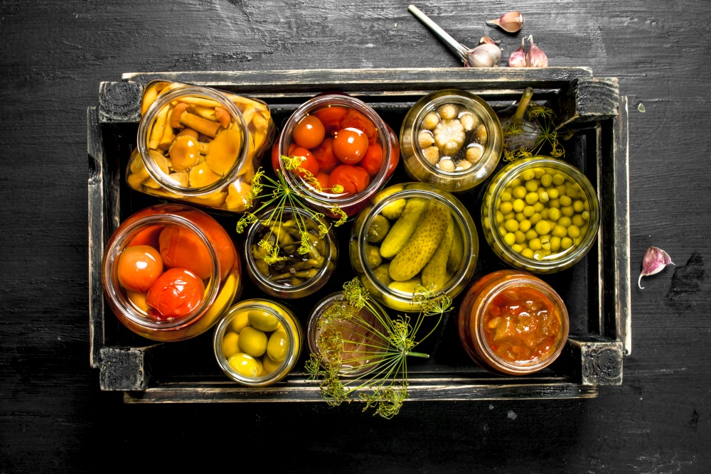 Preserves vegetables in glass jars in an old box. On the black chalkboard.. Preserves vegetables in glass jars in an old box.