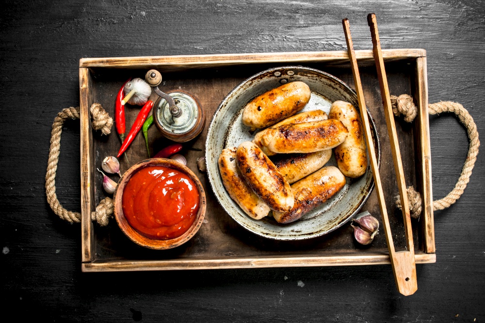 Sausages in a frying pan with sauce on a wooden tray. On the black chalkboard.. Sausages in a frying pan with sauce on a wooden tray.