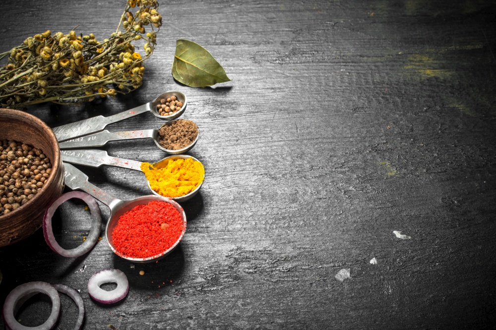 Spices and herbs with measuring spoons. On the black chalkboard.. Spices and herbs with measuring spoons.