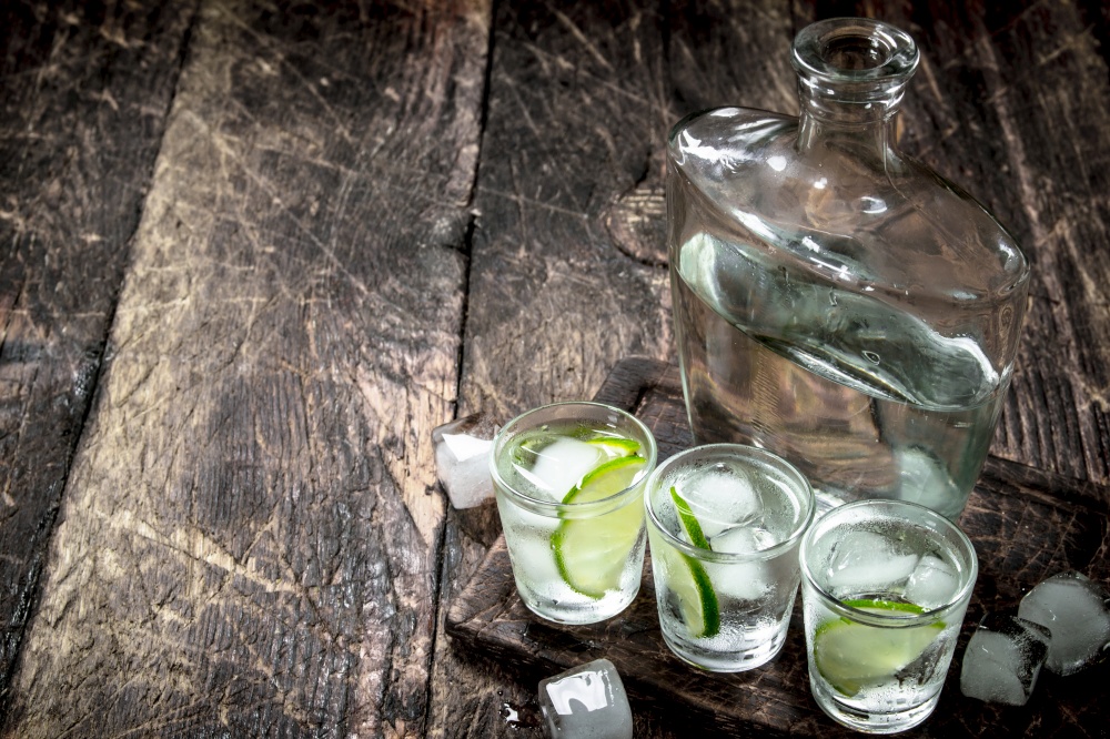 Vodka shots with lime and ice on the board. On a wooden background.. Vodka shots with lime and ice on the board.