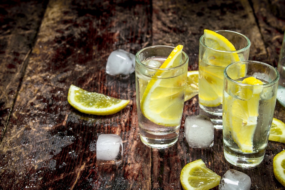 Vodka shots with ice and lemon. On a wooden background.. Vodka shots with ice and lemon.