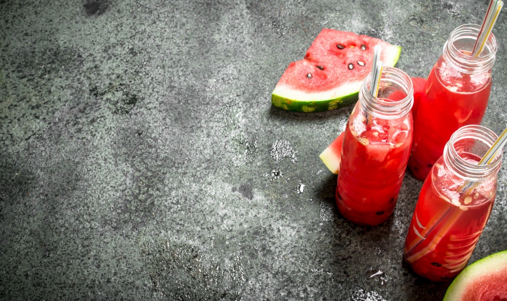 Watermelon juice in bottles with straws. On a rustic background.. Watermelon juice in bottles with straws.