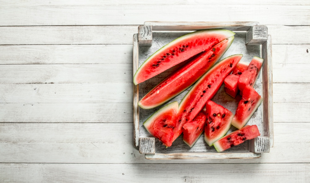 Pieces of sliced ripe watermelon in a box. On a white wooden table.. Pieces of sliced ripe watermelon in a box.